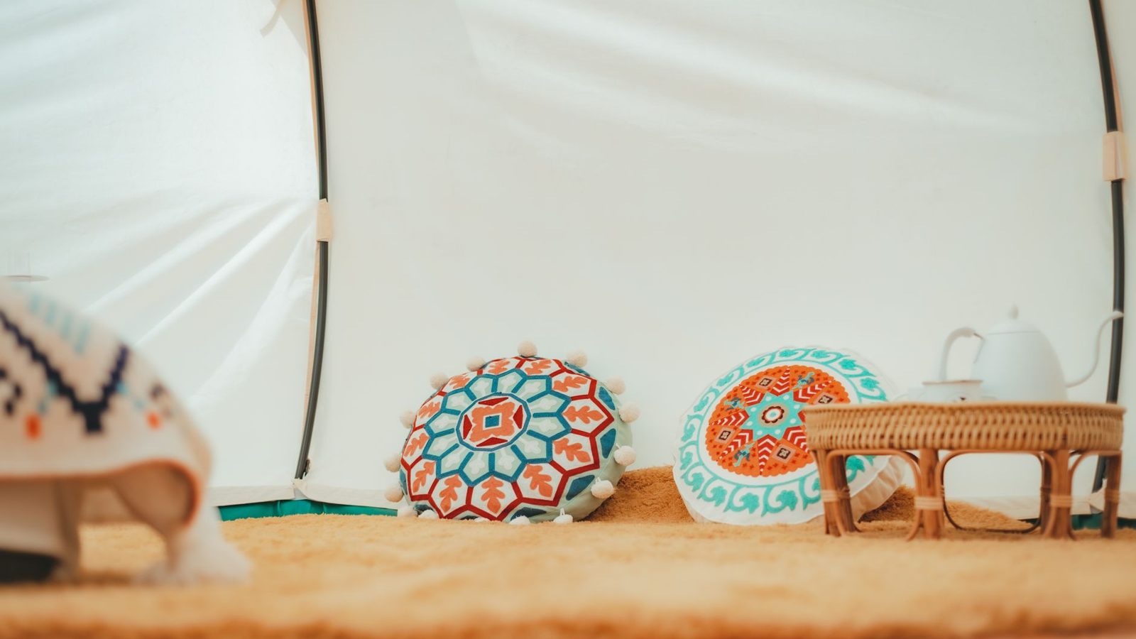 A cozy tent interior featuring vibrant patterned pillows and a teapot on a woven table.