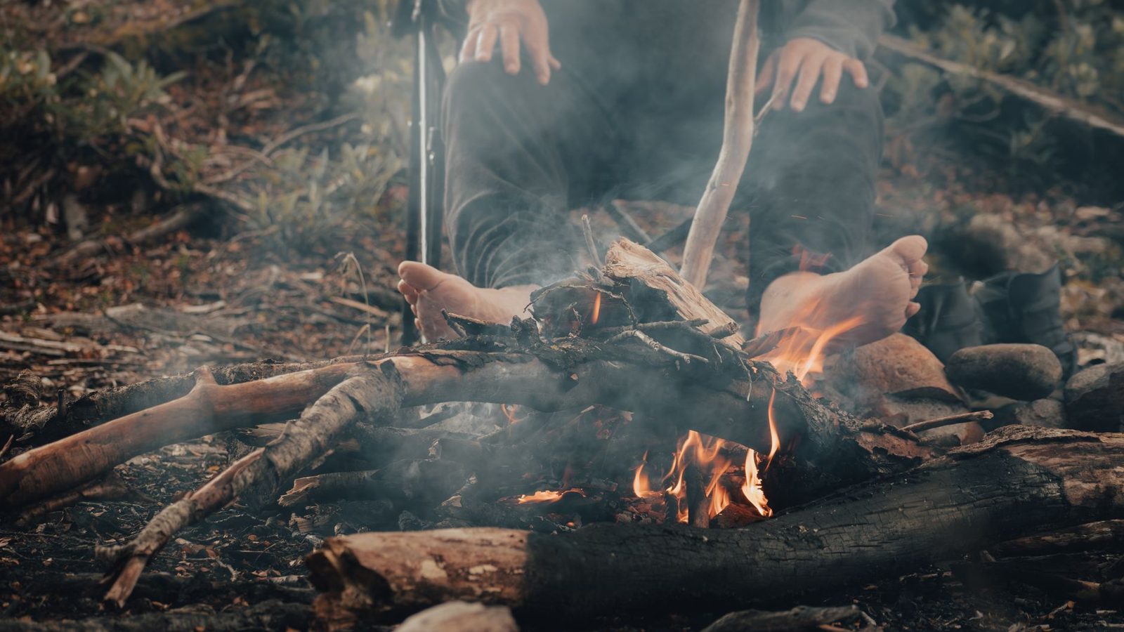 A man seated by a campfire outdoors, enjoying a peaceful time with nature.