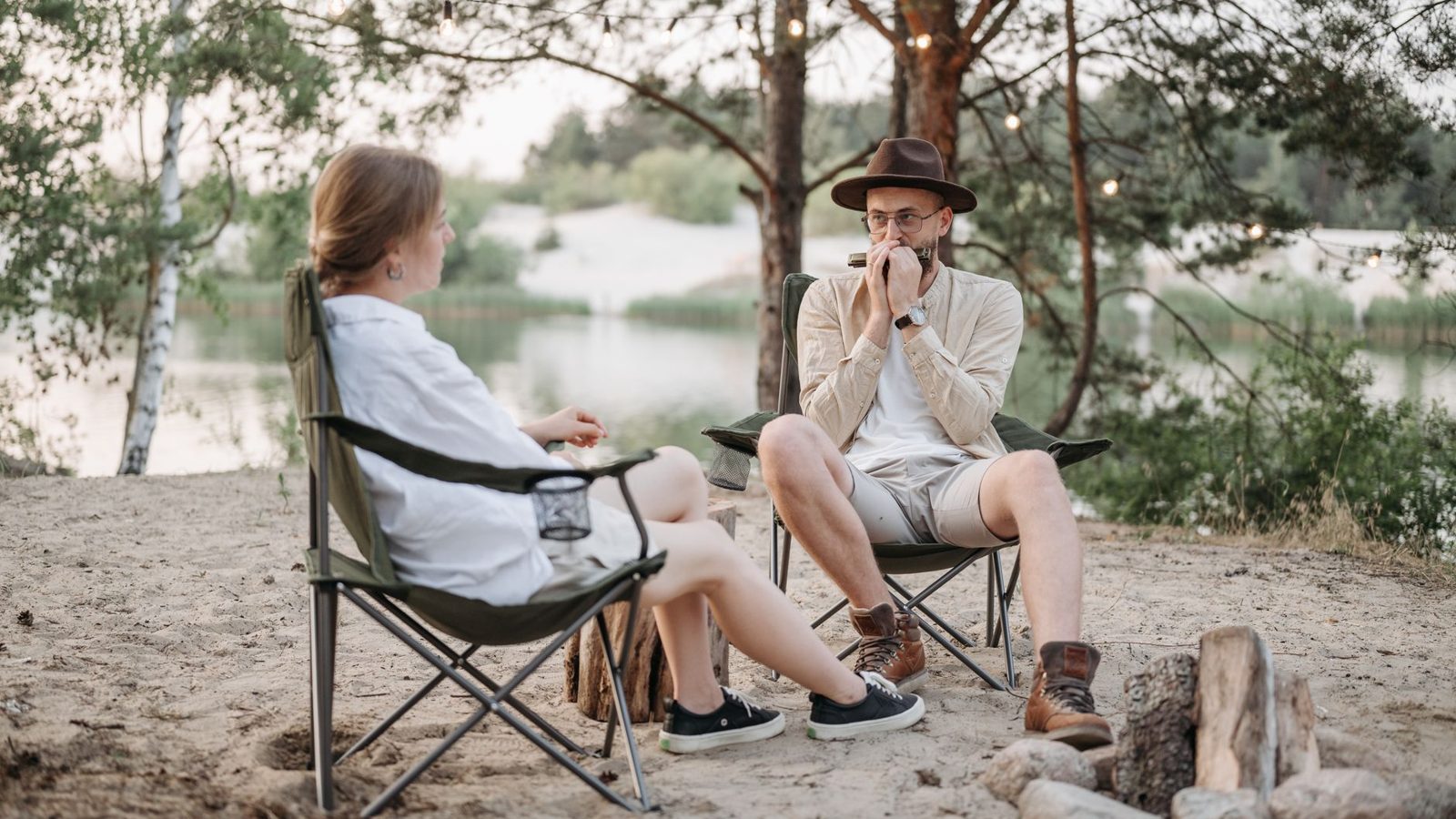 Relaxing outdoor scene with a couple near a campfire by the lake, playing harmonica.