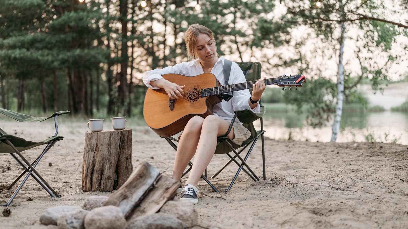 A serene camping scene with a woman playing guitar by a bonfire, surrounded by nature.